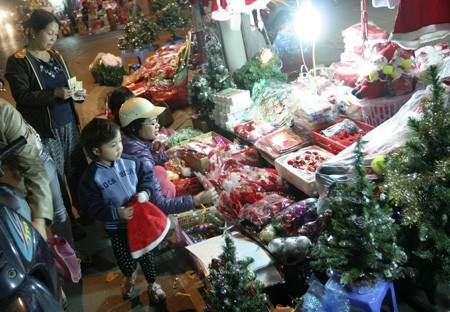 Một em nhỏ tỏ ra vui vẻ khi được người lớn mua cho chiếc mũ màu đỏ của ông già Noel.